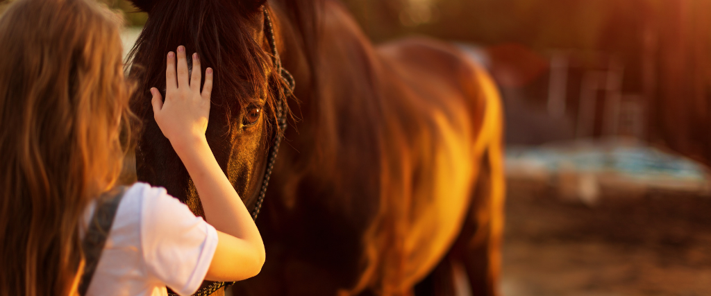 Young blonde girl stroking a brown horse.